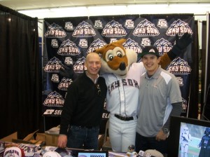 Director of Corporate Sales Chris Phillips and Group Sales Manager Drew Trujillo pose with Sox in front of the Sky Sox booth at the Home and Landscaping Show. 